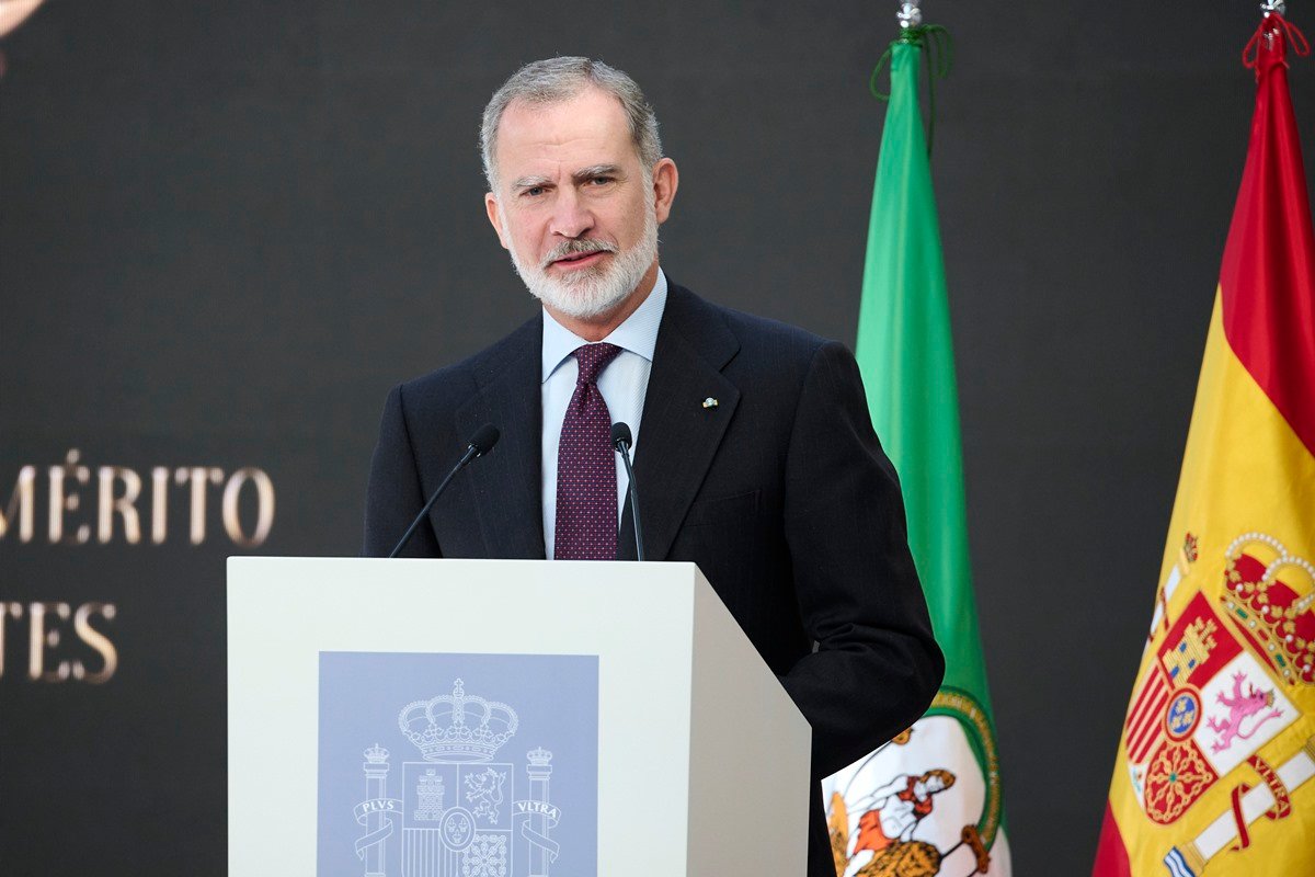 Foto colorida de homem falando ao microfone. Ao lado, há a bandeira da Espanha - Metrópoles