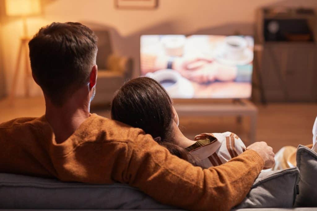 Casal sentado em sofá assistindo TV numa sala