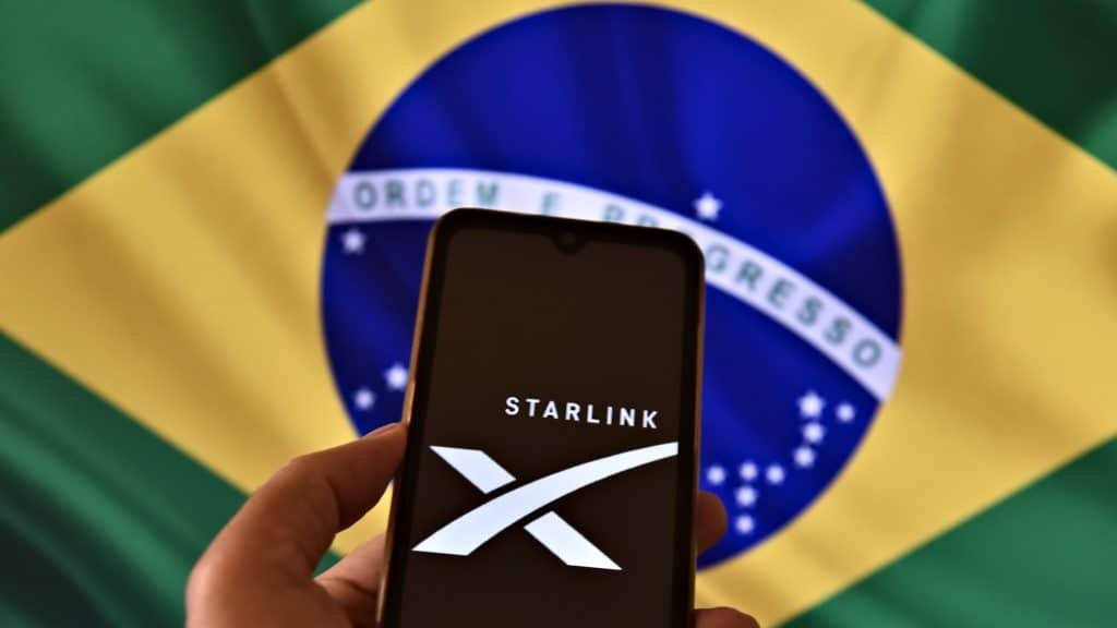 Pessoa segurando celular com logotipo da Starlink na tela na frente de bandeira do Brasil