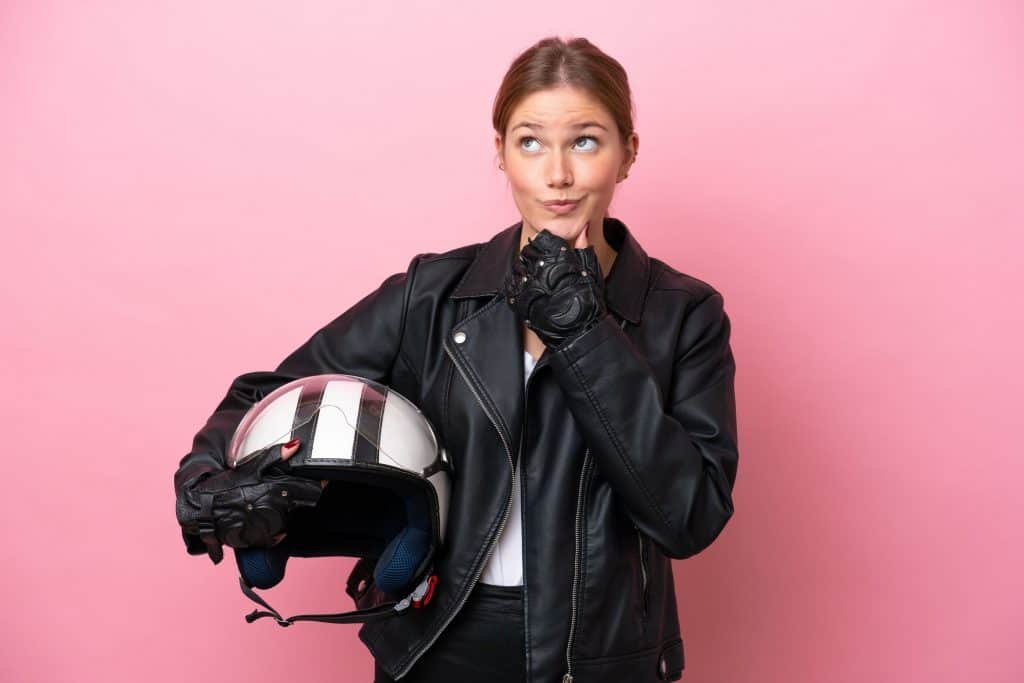 Imagem mostra mulher jovem segurando um capacete e com expressão pensativa de dúvida