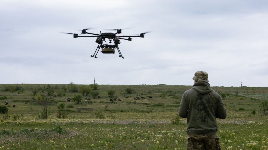 Drone militar voa no céu e um soldado está por perto e o controla