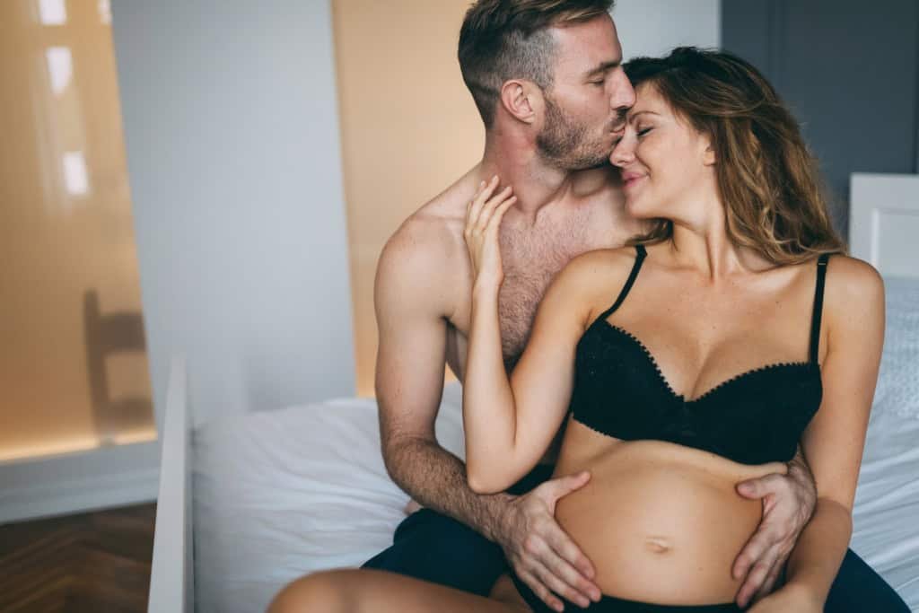 Imagem mostra momento de intimidade entre casal, com homem beijando a testa da mulher grávida e com as mãos na barriga dela